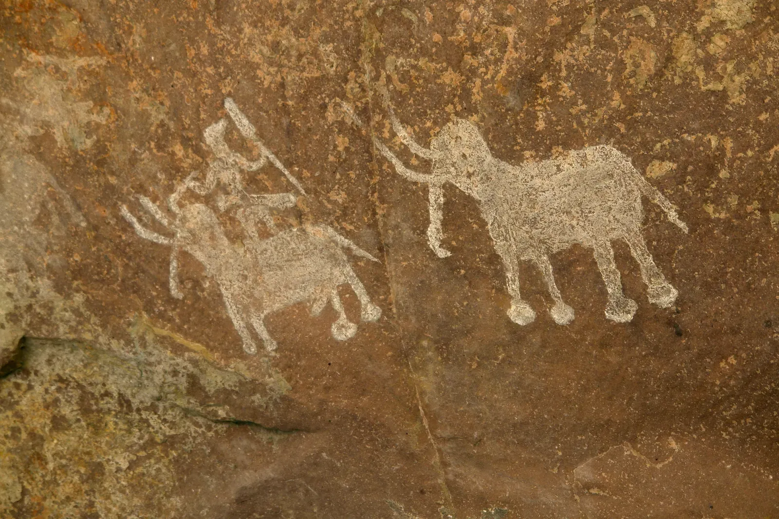 A weathered rock panel at Bhimbetka showing faded ochre paintings of animals and human figures.